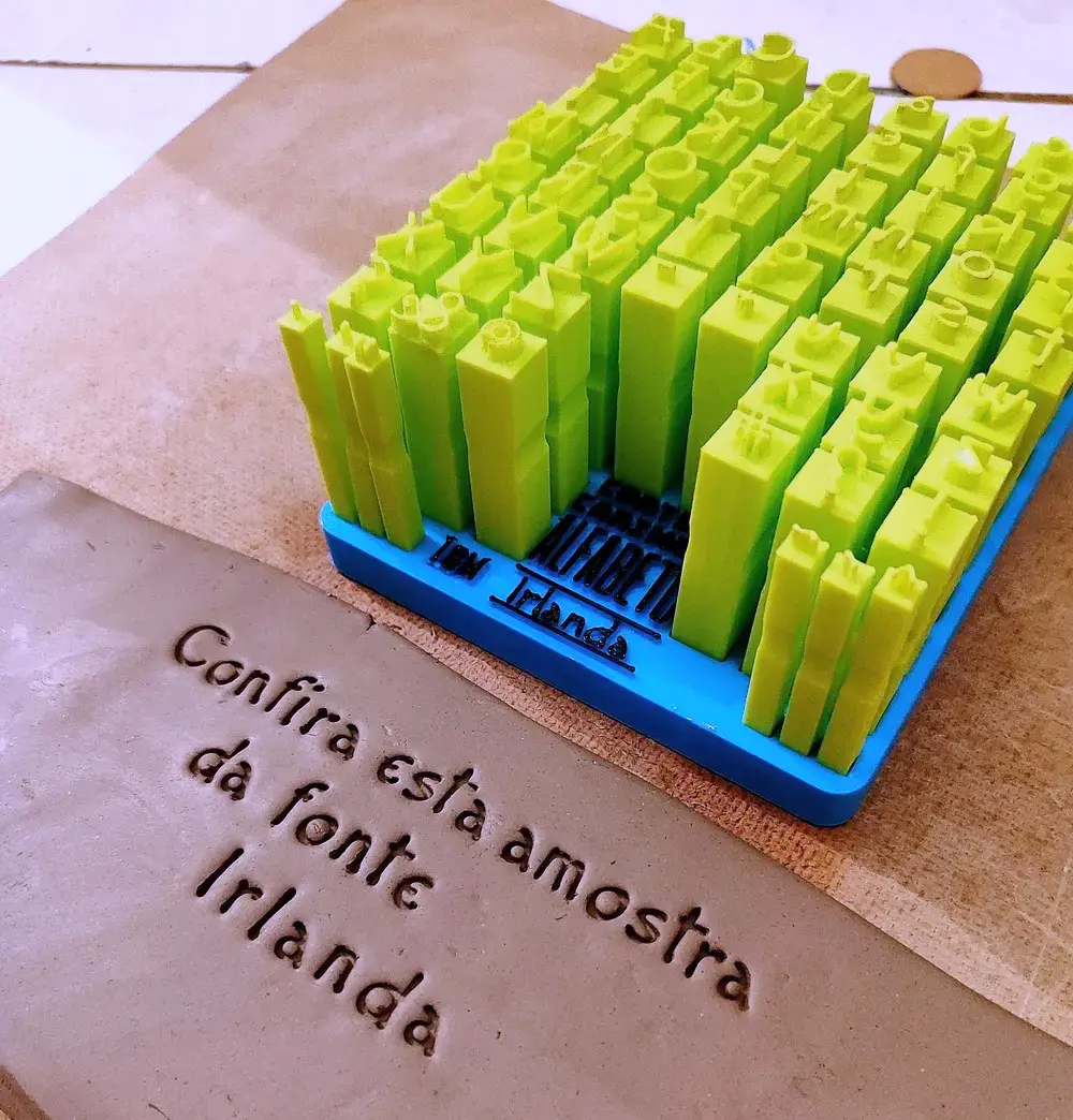 Kit Alfabeto da fonte Irlanda, letras com face verde na base azul, sobre a placa de argila com a frase carimbada